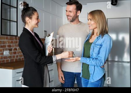 Sicuro sorridente realtor che dà le chiavi della casa alla coppia Foto Stock