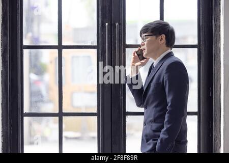 Bell'uomo d'affari che controlla le e-mail sul telefono vicino alla finestra nel monolocale interno loft Foto Stock