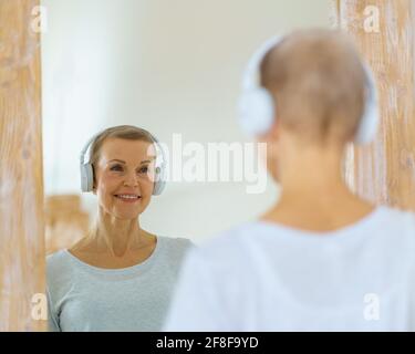 Donna anziana dai capelli grigi che si ammira nello specchio. La donna di mezza età si guarda. Mature bella donna bionda con i capelli di colpo admires riflessione in piedi davanti al grande specchio Foto Stock