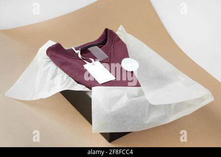 etichetta vuota per dimensioni, logo, istruzioni su pullover borgogna in scatola nera e carta tissue bianca su carta da artigianato beige Foto Stock
