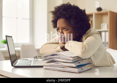 Stanca annoiata giovane donna seduta alla scrivania dell'ufficio e in attesa per la fine della giornata lavorativa Foto Stock