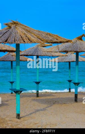 Ombrelloni da spiaggia di paglia che forniscono ombra sulla costa sabbiosa in una giornata estiva soleggiata e limpida a Vama Veche, Romania Foto Stock