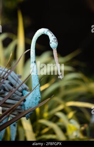 airone ornamentale dipinto di blu con piume di legno in giardino con Cordilina australis a ventaglio "Red Star" Foto Stock