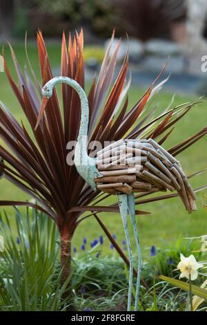 airone ornamentale dipinto di blu con piume di legno in giardino con Cordilina australis a ventaglio "Red Star" Foto Stock