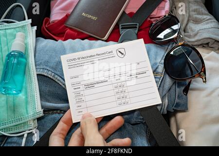 Valigia di imballaggio in epoca pandemica. Viaggiare con maschera facciale, disinfettante per le mani e passaporto per il vaccino. Foto Stock
