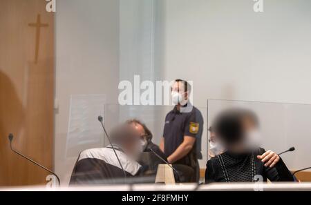 Augusta, Germania. 14 Apr 2021. Una donna e un uomo si siedono nella banchina sotto una croce nella sala della giuria. Gli imputati sono accusati di aver accusato le compagnie di assicurazione di assistenza infermieristica di milioni di persone tramite fatturazione per i servizi di assistenza che non sono stati forniti. Credit: Stefan Puchner/dpa - ATTENZIONE: Gli imputati sono stati pixelated per ordine della difesa/dpa/Alamy Live News Foto Stock