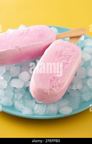 Popsicle di fragole e ghiaccio tritato su sfondo giallo Foto Stock