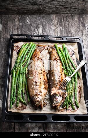 Trota arcobaleno al forno con asparagi e spezie sulla teglia da forno su tavolo di legno Foto Stock