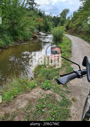 Ciclista fotografata con smartphone. Uomo caucasico senza casco da bicicletta per scattare foto di paesaggio. Attività all'aperto. Tourist scatta foto di un fiume Foto Stock