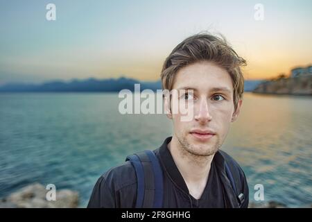 Faccia di serio giovane europeo vicino al mare al tramonto ad Antalya di primavera. Foto Stock