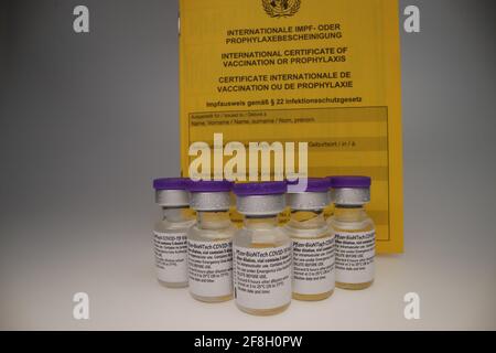 flaconcino di vaccino comirnaty originale disposto in un gruppo davanti di un backrop bianco con certificato di vaccinazione tenuto dietro di loro Foto Stock