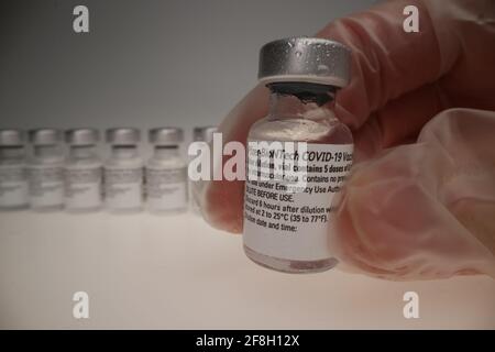 flaconcino di vaccino comirnaty originale disposto in un gruppo davanti di un backrop bianco che è preso da una mano indossare un guanto monouso Foto Stock
