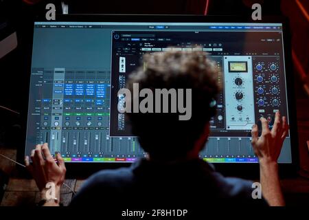 Uomo che lavora in studio musicale utilizzando un grande schermo del computer da dietro Foto Stock