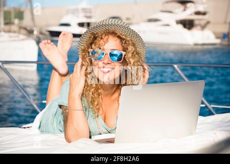 Giovane bella donna adulta sorriso e utilizzare il computer portatile all'aperto adagiarsi sul ponte di uno yacht - viaggio e vacanza estiva stile di vita vacanza e mod Foto Stock