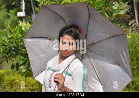 Adolescente indiano bengalese ragazza indossando bianco cotone salwar tenendo un ombrello in una fattoria di villaggio, focalizzazione selettiva Foto Stock