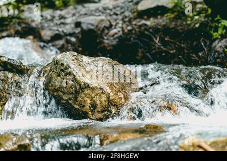 Primo piano del flusso rapido e pulito che scorre sulle rocce. Il fiume di montagna scorre giù e spruzzi Foto Stock