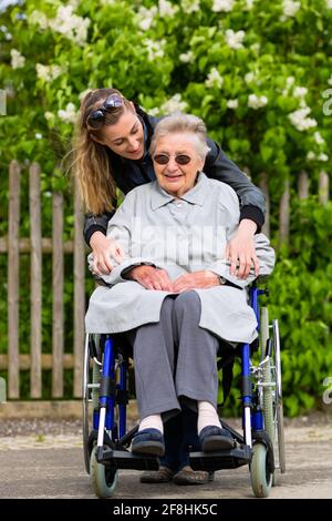 Giovane donna è in visita a sua nonna nella Casa di cura avente una passeggiata con qui in una sedia a rotelle Foto Stock