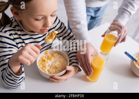 ragazza che mangia fiocchi di mais vicino al padre e bicchieri d'arancia succo Foto Stock