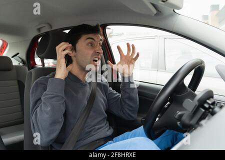 L'uomo furioso gesticulates con le mani incastrate in ingorgo di traffico. Il pazzo conducente urla disperatamente dall'auto. Stress, concetto di ora di punta del traffico Foto Stock