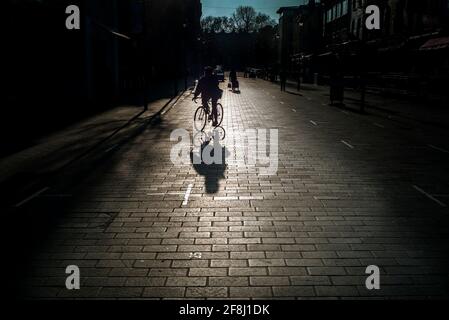 Silhouette di uomo irriconoscibile in bicicletta, ombre su una strada acciottolata, Inverness Street Camden, Londra UK Foto Stock