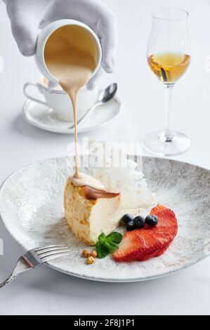 Cheesecake con fragole fresche e mirtilli su piatto bianco e. il latte di caffè sono sul tavolo nel caffè e. bicchiere di cognac Foto Stock