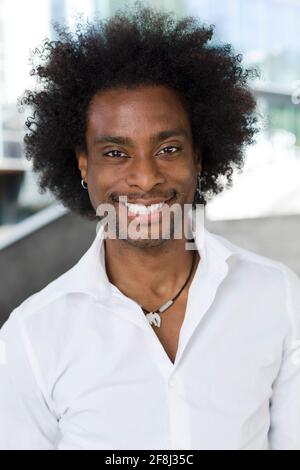 Ritratto verticale del giovane nero felice e sorridente. Ha i capelli afro ed è vestito casualmente in una camicia bianca. Foto Stock