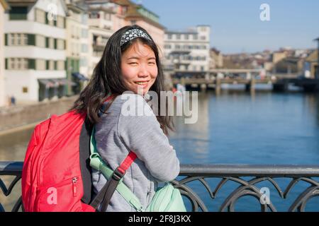 Donna asiatica zaino in spalla in giro in Europa - giovane felice e. Bella ragazza coreana con zaino con vista sulla città e sul fiume dal ponte durante le vacanze in Foto Stock