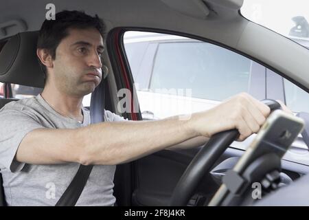 Uomo stressato che ruffa e gonfia durante la guida. Driver sconsiderata che perde pazienza in ingorgo di traffico Foto Stock