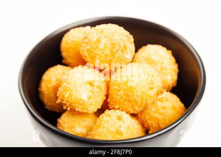 Palline di formaggio in un recipiente nero isolato su bianco dall'alto. Palle di formaggio dorato soffiato come classico spuntino per bambini su sfondo di legno Foto Stock