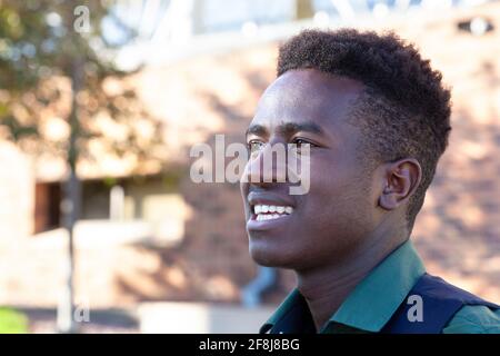 Un bel giovane studente nero sorridente si trova di fronte il suo collegio Foto Stock