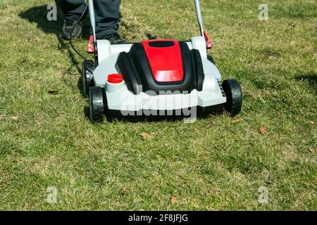 Aerazione con scarificatore. Utilizzando uno scarificatore in giardino per migliorare la qualità del prato in primavera. Un uomo lavoratore, giardiniere che opera l'aerazione del suolo Foto Stock