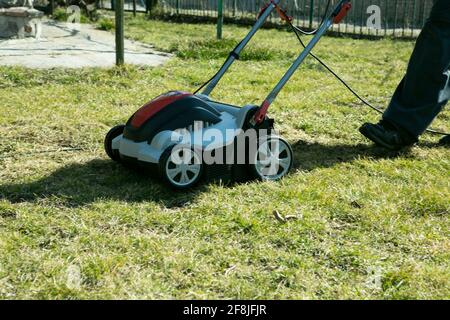 Aerazione con scarificatore. Utilizzando uno scarificatore in giardino per migliorare la qualità del prato in primavera. Un uomo lavoratore, giardiniere che opera l'aerazione del suolo Foto Stock