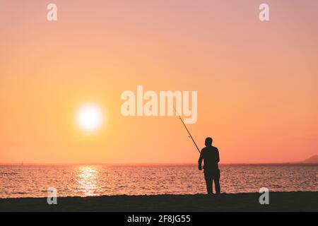 Silhouette di uomo in pesca onde sulla spiaggia al tramonto Foto Stock