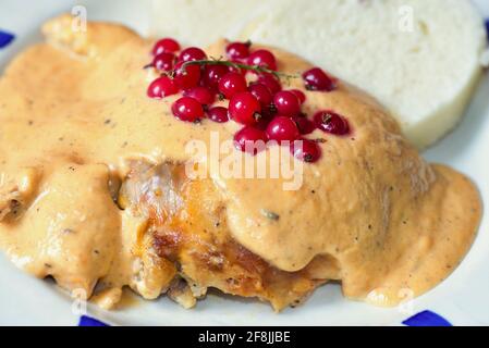 Coniglio arrosto con salsa di crema vegetale decorata con curry rosso, gnocchi su piatto bianco. Foto Stock