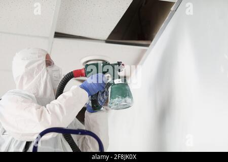 Lavoratore di costruzione in tuta protettiva e respiratore pittura parete con pistola a spruzzo Foto Stock