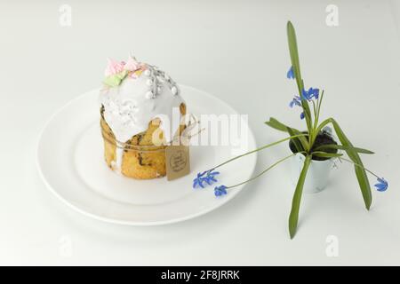 Torta di Pasqua ortodossa su un piatto bianco con primavera blu fiorire in una vista laterale del vaso con un angolo sopra il tavolo Foto Stock