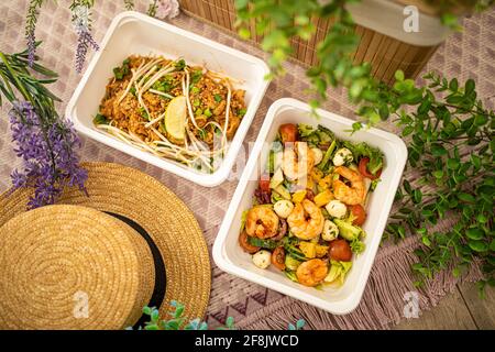 Insalata di gamberi, pad asiatico thai.composition con arredamento naturale. Consegna di cibo concept in ufficio o per picnic in piatti di plastica monouso. Foto Stock