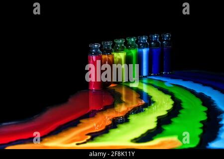 Moderna natura morta raffigurante sette colori di arcobaleno su sfondo nero con riflessione su un tavolo di vetro. Sette bottiglie colorate con sette ruscelli Foto Stock