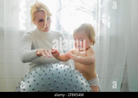 La mamma è impegnata in ginnastica con il bambino su una palla gonfiabile. Fitball, ginnastica per un bambino. Foto Stock