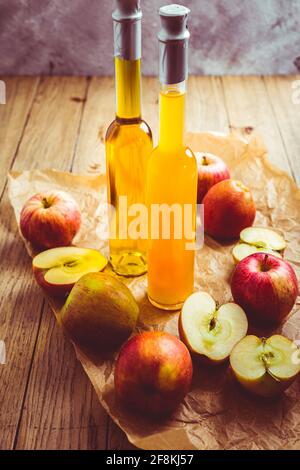 Succo di mela con aceto di mela in bottiglie e mele fresche su sfondo di legno Foto Stock