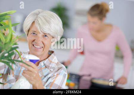 donna anziana felice che lavora alla sua casa giardino annaffiatura piante Foto Stock