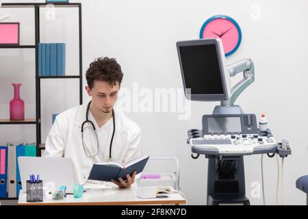 Un giovane medico primario esamina le voci del calendario dei libri sui suoi pazienti. L'ufficio del medico Foto Stock