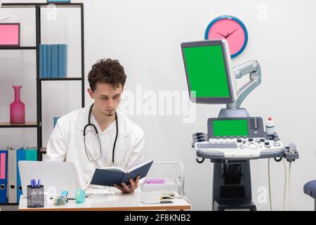 Un giovane medico primario esamina le voci del calendario dei libri sui suoi pazienti. Schermo verde Foto Stock