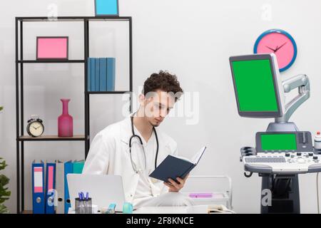 Un giovane medico primario esamina le voci del calendario dei libri sui suoi pazienti. Schermo verde Foto Stock