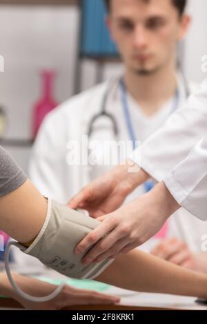 Vista ravvicinata di un infermiere che posiziona un monitor della pressione sanguigna sul braccio di un paziente. Medico generico. Studio medico Foto Stock