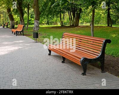 Vicolo vuoto con nuove panchine e piastrelle grigie lastricate nel parco della città in bella estate soleggiato giorno a Kiev, Ucraina Foto Stock