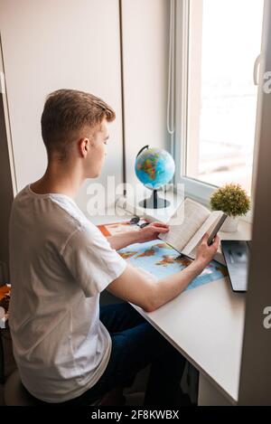 Concetto di viaggio. Giovane ragazzo dietro un computer portatile, lavoro online, turismo e viaggi Foto Stock