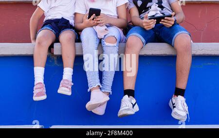 Bambini caucasici seduti sui bleachers con i loro dispositivi mobili e le cuffie, condividendo momenti di risate e conversazioni. Foto Stock