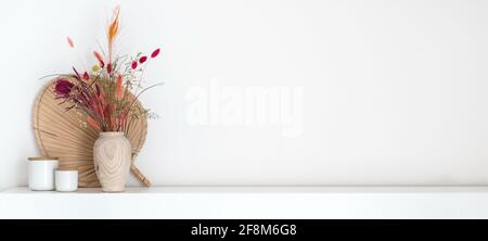 Intestazione di bouquet di fiori secchi colorati in stile boho vaso di legno in piedi su un ripiano bianco con un sacco di spazio di copia Foto Stock