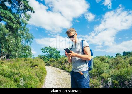 Young Male turista con zaino utilizzando l'app di navigazione smartphone durante le escursioni a piedi nella foresta estiva. Tecnologia nella vita quotidiana. Viaggi locali Foto Stock